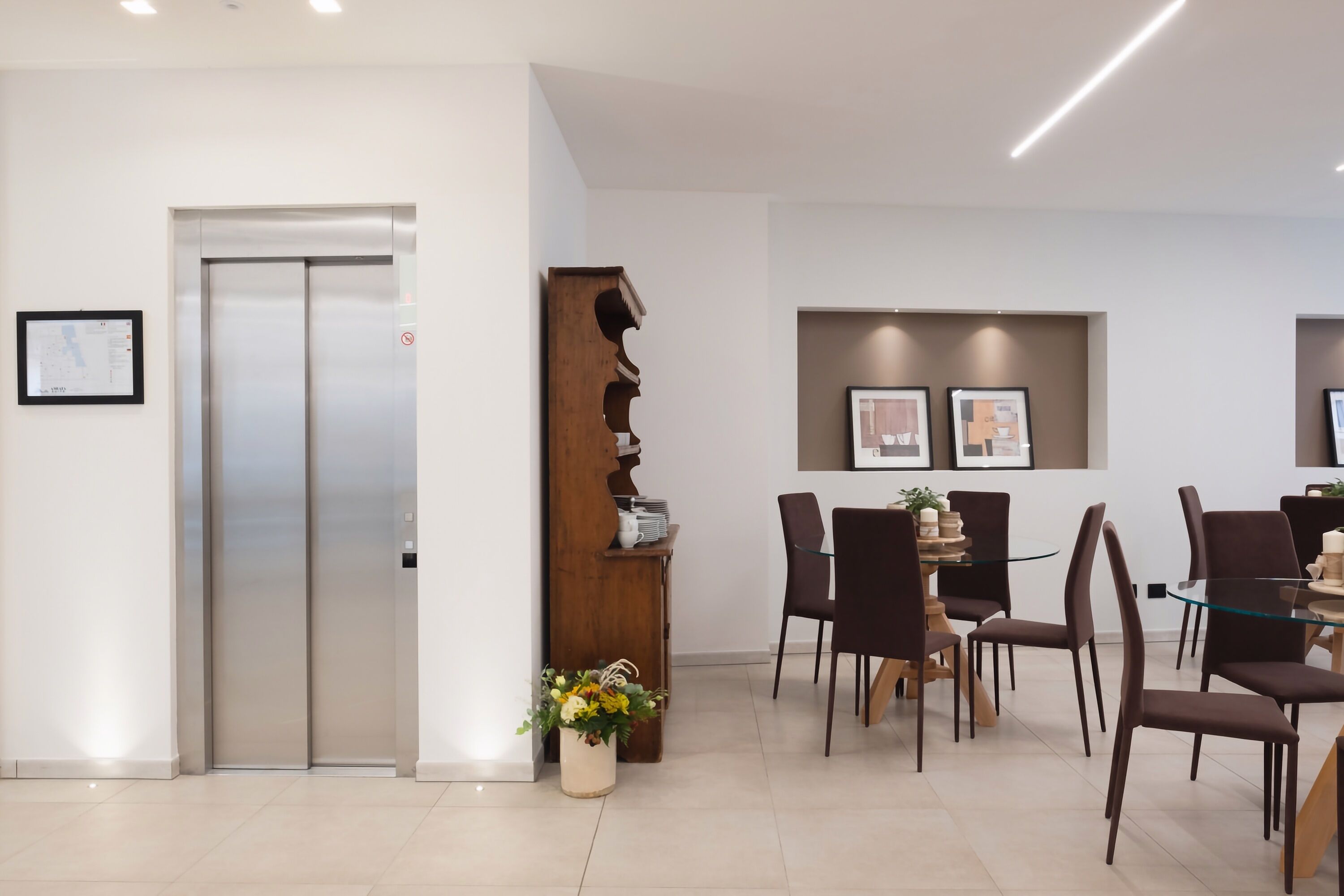 A modern interior with a dining area, a wooden bookshelf, and a wall-mounted elevator.