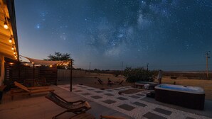 Une terrasse extérieure avec des chaises longues, un jacuzzi et un ciel étoilé.