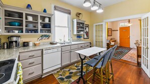A kitchen with white cabinets, a dining table with chairs, and a window with blinds.