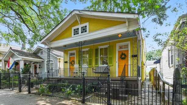 A yellow house with a porch, a black iron fence, and a wreath on the door.