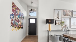Un corridoio con pavimento in legno, una porta nera, un lampadario e una parete decorata con diversi quadri e un quadro astratto dai colori vivaci.