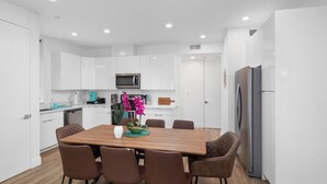 A modern kitchen with white cabinetry, a wooden dining table, and six brown chairs. - Luminousness Reflection 4B2.5B Home (Torrance)