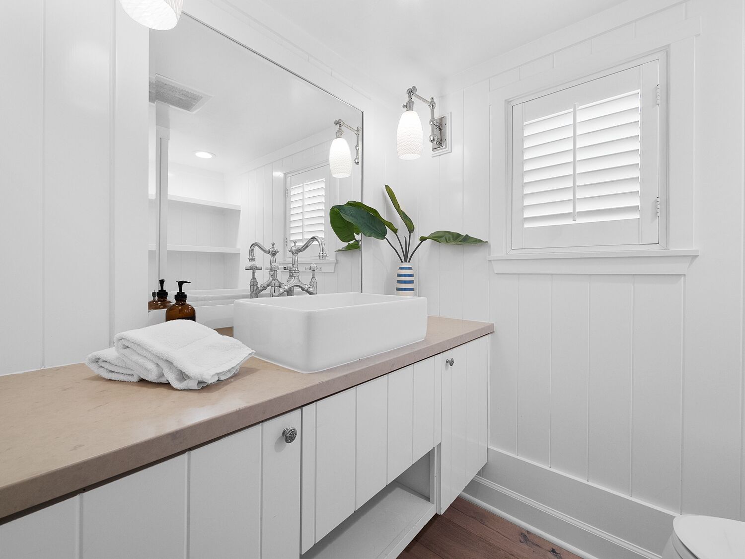 A modern bathroom with a white vanity, a large mirror, a white sink, and a potted plant.