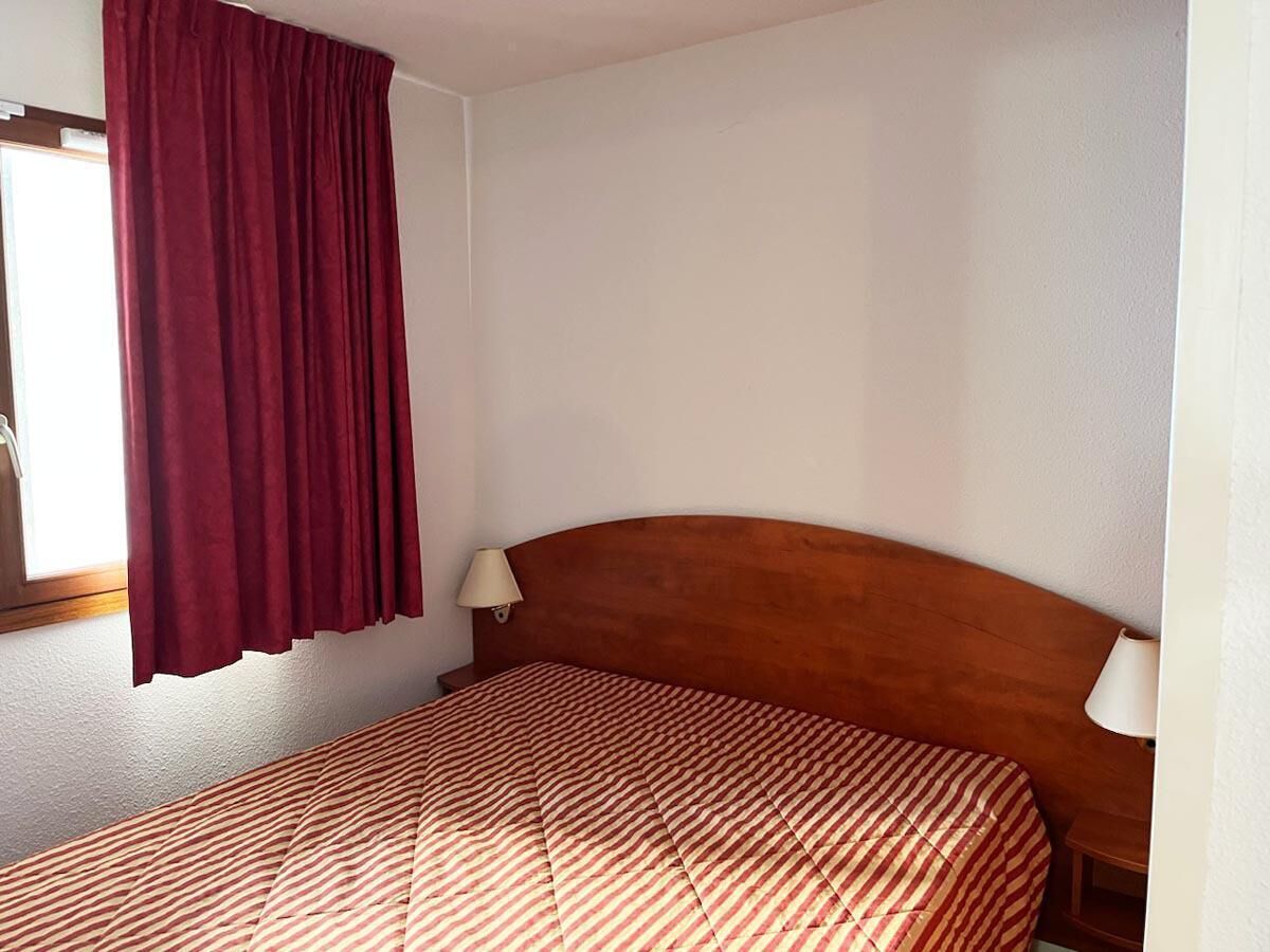 Een kamer met een houten hoofdbord, twee bedlampen en een raam met rode gordijnen.