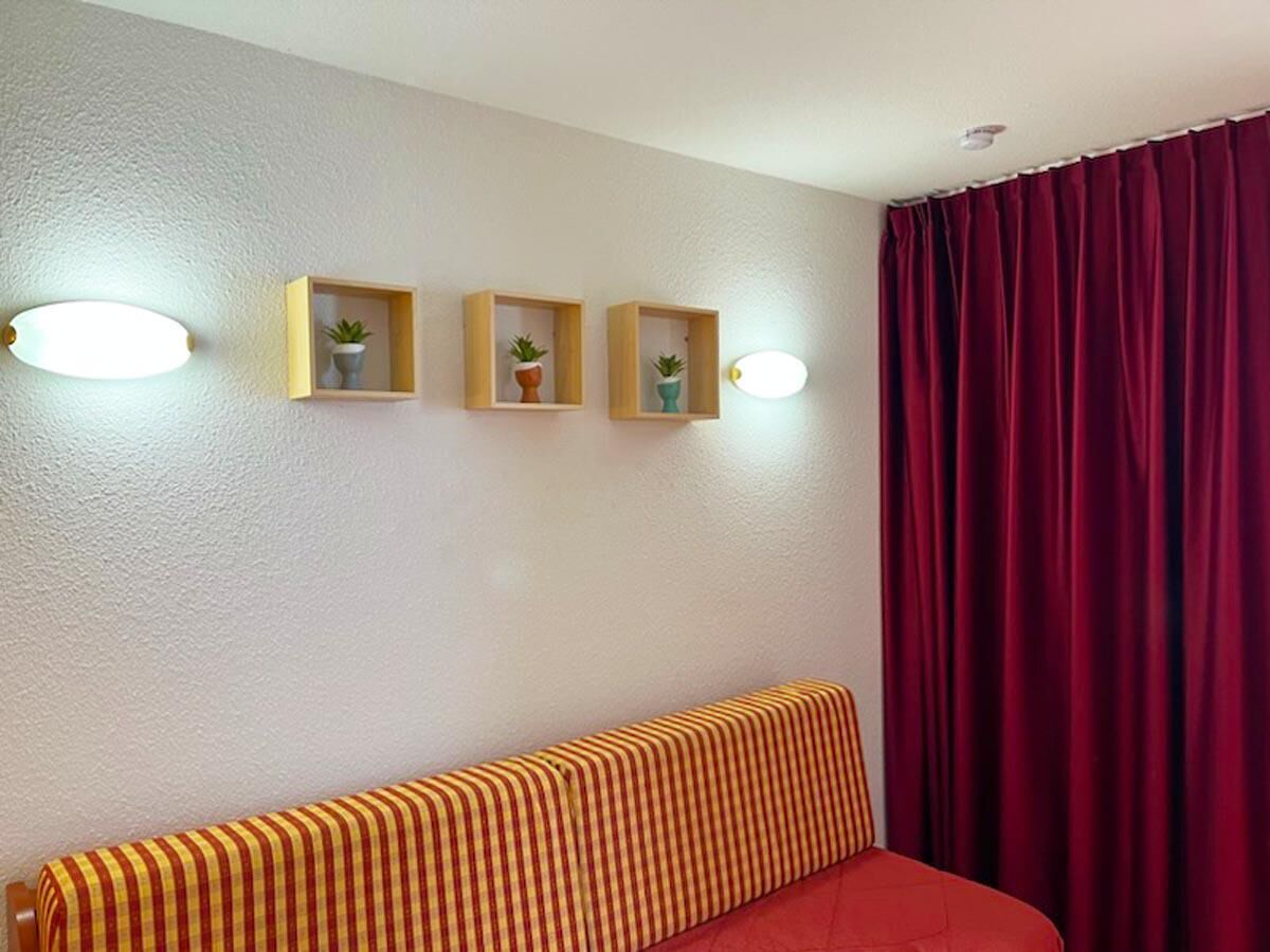 A room with a striped sofa, three wooden shelves with plants, and a red curtain.