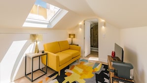 Ein modernes Schlafzimmer im Loft-Stil mit Dachfenster, einem gelben Sofa, einem gemusterten Teppich und einem Fernseher.