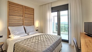 Ein modernes Hotelzimmer mit einem großen Bett, einem Flachbildfernseher, einem Holztisch und einem Balkon mit Blick.