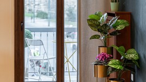 A room with a sliding glass door leading to an outdoor area with a chair and table. There are several potted plants on a stand near the door. - Acropolis Prestige Residence (Athina)