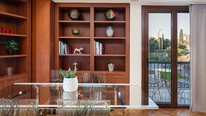 A modern living room with a glass coffee table, wooden bookshelves, and a view of a balcony with outdoor furniture. - Acropolis Prestige Residence (Athina)