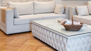 A modern living room with a white sectional sofa, a glass coffee table, and a large abstract painting. - Acropolis Prestige Residence (Athina)