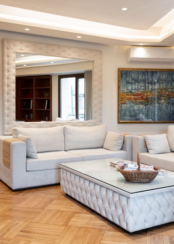 Un salon moderne avec un canapé d’angle blanc, une table basse en verre et un grand tableau abstrait.