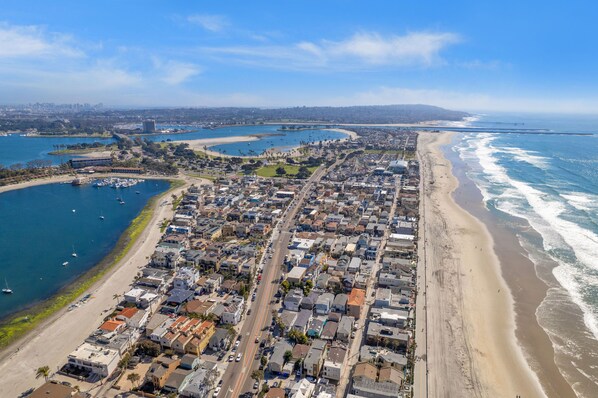 Vista aérea de uma cidade costeira com um porto de iates, praia e área residencial densa.