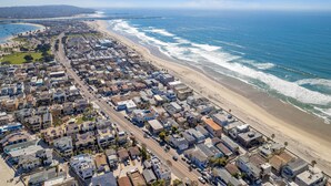 Vista aérea de un pueblo costero con una playa, edificios residenciales y un puente a lo lejos.
