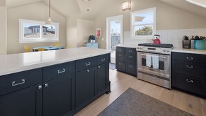 Una cocina moderna con una isla grande, armarios oscuros, electrodomésticos de acero inoxidable e iluminación colgante.