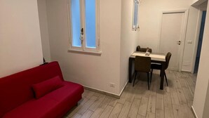 A room with a red sofa, a dining table with chairs, and a window with frosted glass.