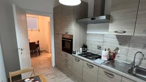 A modern kitchen with light wood cabinets, a stainless steel sink, and a dining area with a wooden table set for two.