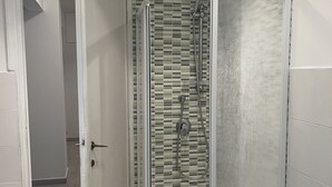 A modern bathroom with a glass-enclosed shower, tiled walls, and a wooden floor.