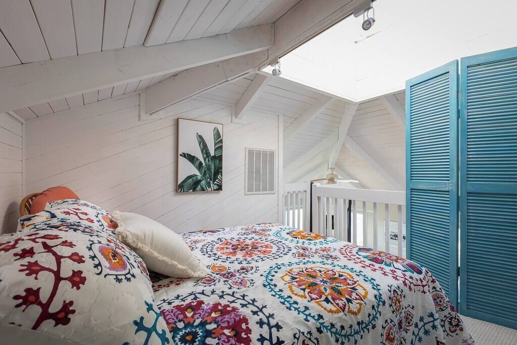 A bedroom with a sloped ceiling, a bed with a colorful floral bedspread, a white radiator, and a blue shutter door.