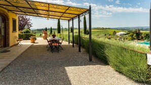 Een overdekt terras met een tafel, stoelen, een pergola en uitzicht op het landschap.