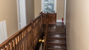 Un escalier en bois avec une rampe, une fenêtre avec des stores et un extincteur sur le palier.