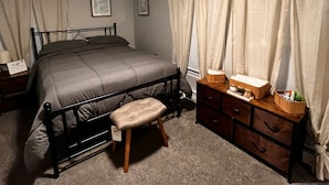 A bedroom with a bed, a nightstand, a dresser, and a small stool. - Beautiful cozy2 bedrooms located in a safe community just minutes from downtown. (East Hartford)