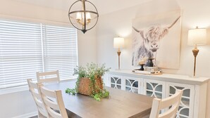 Ein Esszimmer mit Holztisch, weißen Stühlen, einer weißen Schrank mit Glastüren, einem gewebten Korb mit Grünpflanzen und einem Gemälde eines Jaks.