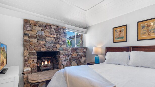 A bedroom with a stone fireplace, a bed with white bedding, and two framed pictures on the wall. - La Jolla Ocean Dream - Amazing Location, Walk to the Beach, Dog Friendly! (La Jolla)