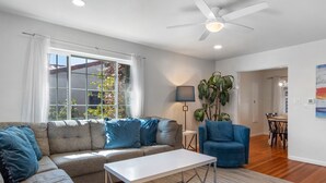 A modern living room with a sectional sofa, a coffee table, a blue armchair, a floor lamp, and a ceiling fan. - La Jolla Ocean Dream - Amazing Location, Walk to the Beach, Dog Friendly! (La Jolla)