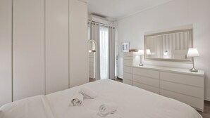 A hotel room with a large bed, a dresser, a mirror, and a door leading to another room. - Belva Blue Glyfada Modern 2BR Walk to Ctr & Beach (Glifada)