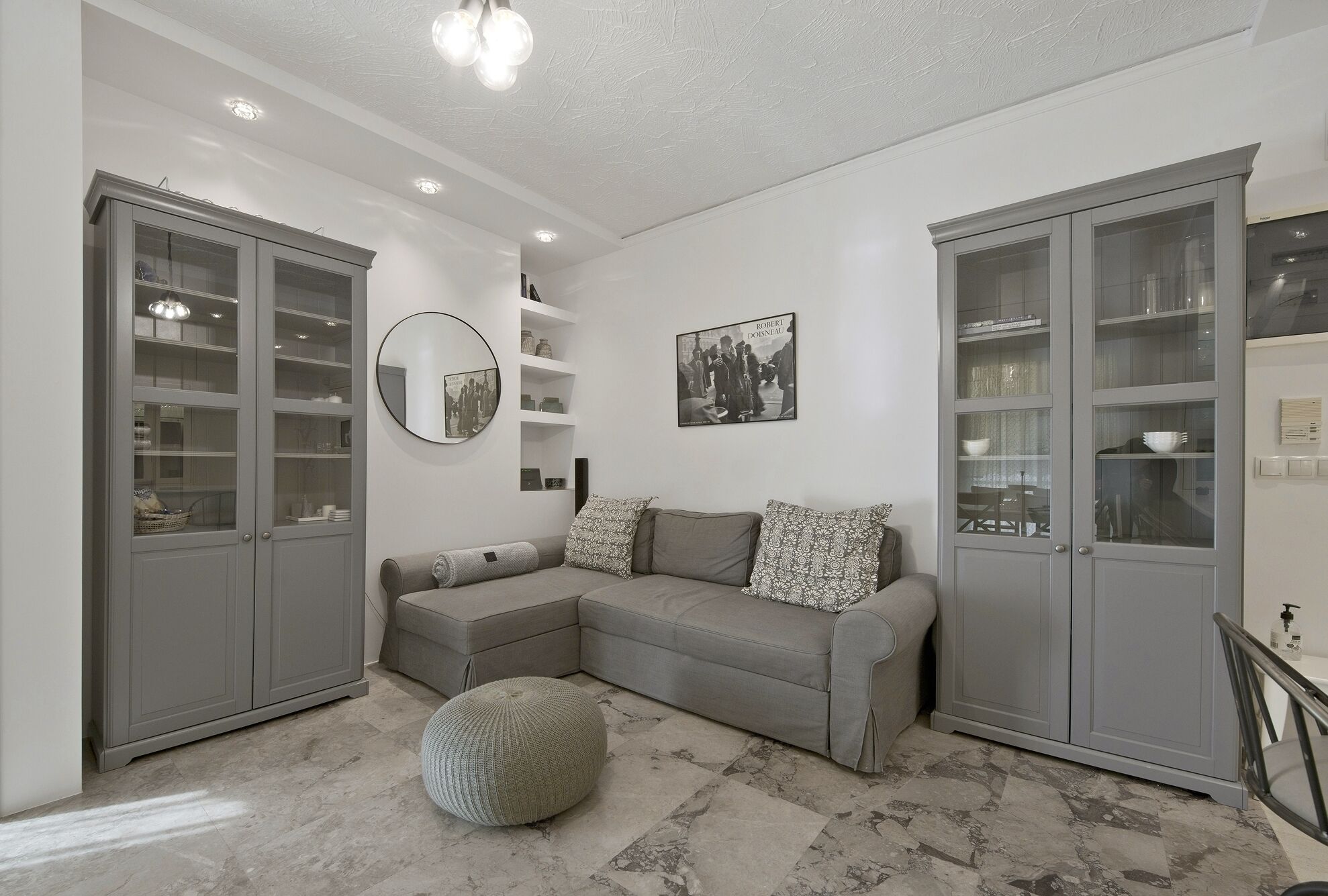 A modern living room with a grey sectional sofa, a round mirror, and built-in glass-fronted cabinets.
