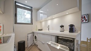 A compact kitchen with a built-in washing machine, a coffee maker, and a dishwasher. - Sea Breeze Spacious Apt near Vouliagmeni Beach (Vouliagmeni)