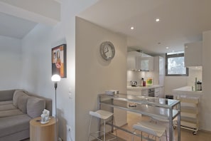 Une cuisine moderne avec un coin repas vitré, des meubles blancs et une horloge au mur.