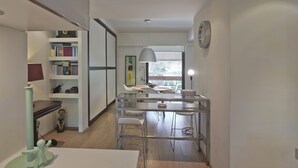 A modern kitchen with a dining area, a bookshelf, and a clock on the wall. - Sea Breeze Spacious Apt near Vouliagmeni Beach (Vouliagmeni)