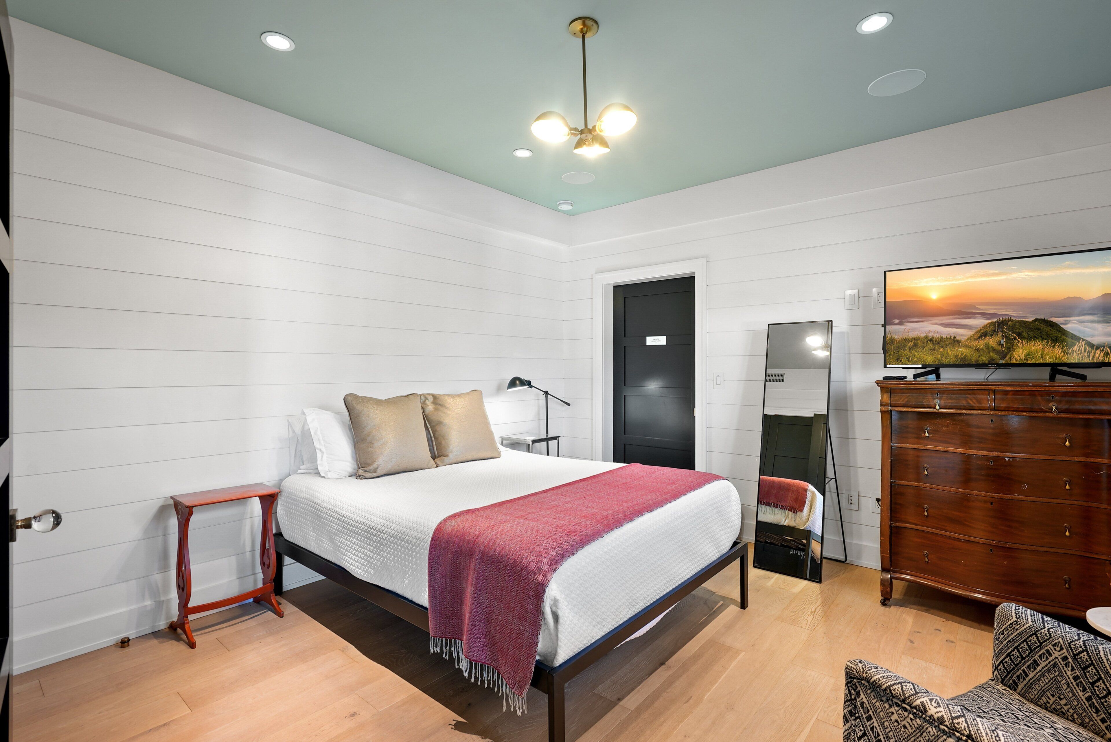 A bedroom with a bed, a dresser, a TV, and a door.