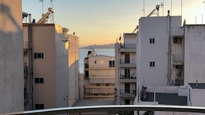 A view of a residential area with buildings, some with balconies and satellite dishes, and a body of water in the distance. - Ella Suite Piraeus Stylish St, Balcony & Sea View (Piraeus)