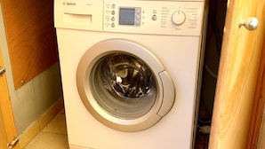 A Bosch washing machine installed under a wooden cabinet in a room with tiled flooring. - Ella Suite Piraeus Stylish St, Balcony & Sea View (Piraeus)