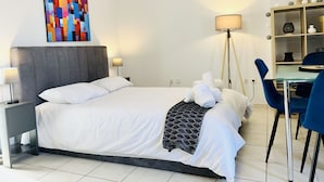 A modern hotel room with a large bed, a bedside table, a lamp, a floor lamp, a desk with chairs, and a colorful abstract painting on the wall. - Ella Suite Piraeus Stylish St, Balcony & Sea View (Piraeus)