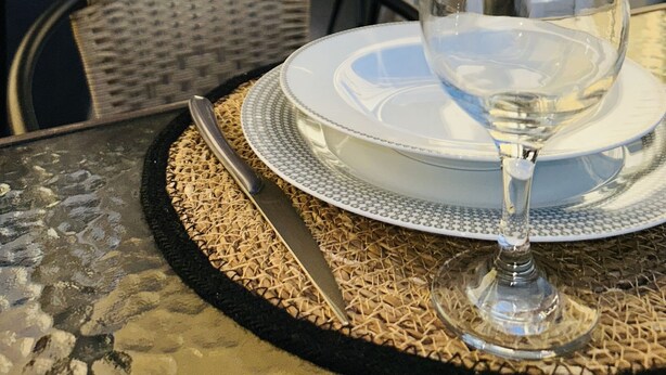 A dining table with a glass, plate, and cutlery set on a woven placemat. - Ella Suite Piraeus Stylish St, Balcony & Sea View (Piraeus)