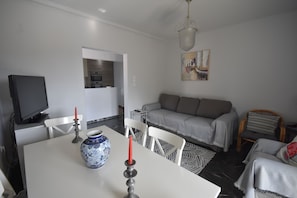 A modern living room with a dining table, a sofa, and a television. - VillaVita Modern 3BR,Garden & BBQ, Walk to Beach (Kalyvia Thorikou)