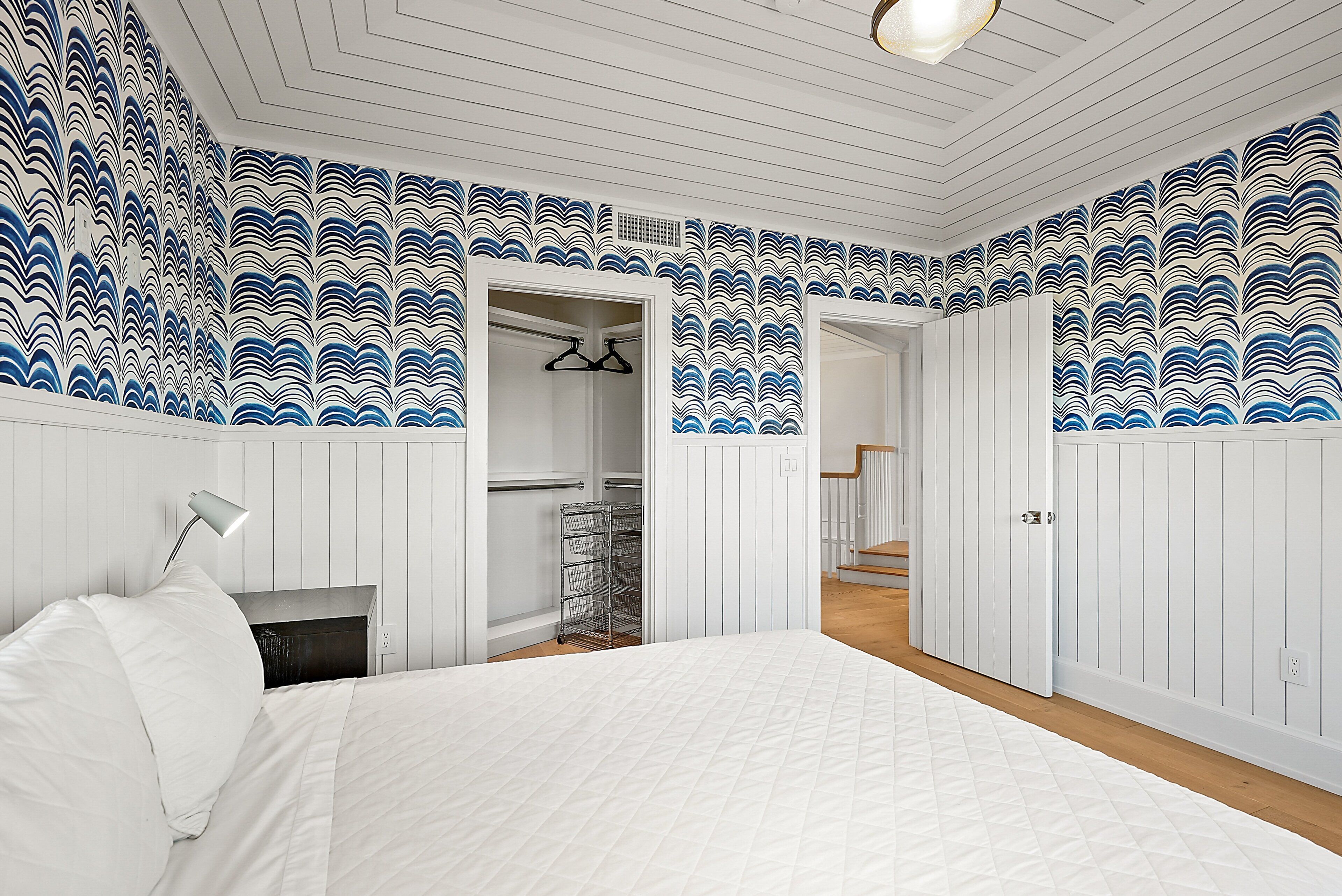 A bedroom with a bed, a nightstand, a hanging lamp, a closet, and a door leading to a staircase.