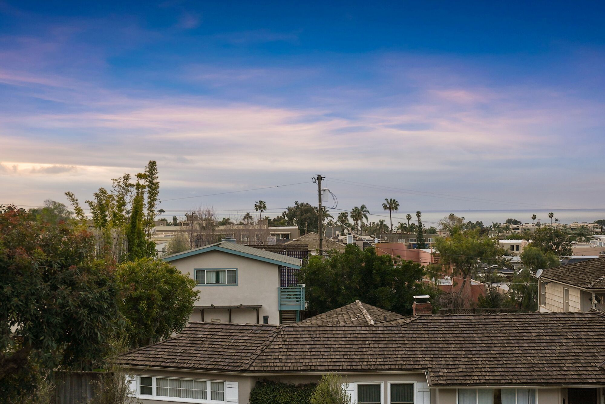 A residential area with houses, some with tiled roofs, and palm trees in the background.