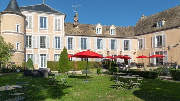 Une cour dotée d’un espace extérieur aménagé avec des sièges, ainsi qu’un bâtiment orné d’une tourelle et de nombreuses fenêtres.