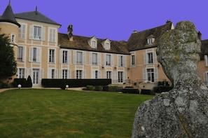 Un grand immeuble à étages, doté d’une façade symétrique et d’une entrée centrale avec un escalier.
