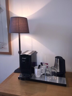 Een koffiehoek met een koffiezetapparaat, kopjes en een glazen karaf op een dienblad.