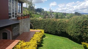 Uma casa com fachada de pedra, um pátio ladrilhado e um jardim bem cuidado com flores amarelas e grama verde.
