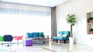 A modern hotel lobby with a large window, a sofa, a coffee table, and colorful chairs.