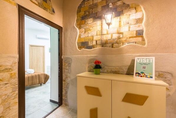 A hotel reception area with a stone wall, a bed in the background, and a sign on the counter.