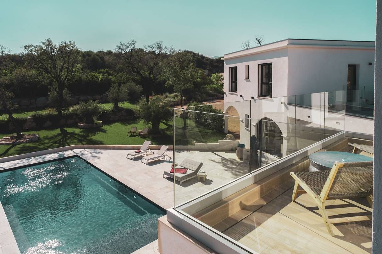 A modern house with a glass balcony overlooking a swimming pool and a garden.