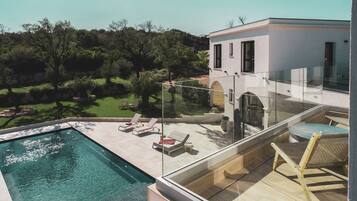 A modern house with a glass balcony overlooking a swimming pool and a garden.