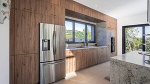 A modern kitchen with wooden cabinets, stainless steel appliances, a marble countertop, and a large window offering a view of greenery. - Villa Blue Pearl, 10 pers, piscine chauffée, 10 minutes plage à pieds (SAINTE LUCIE DE PORTO VECCHIO)